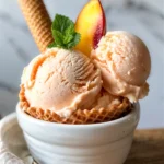 Creamy homemade peach ice cream in a waffle cone with fresh peach slices