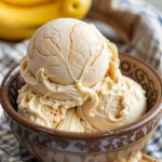 A scoop of creamy no churn banana pudding ice cream in a bowl with vanilla wafers and banana slices.