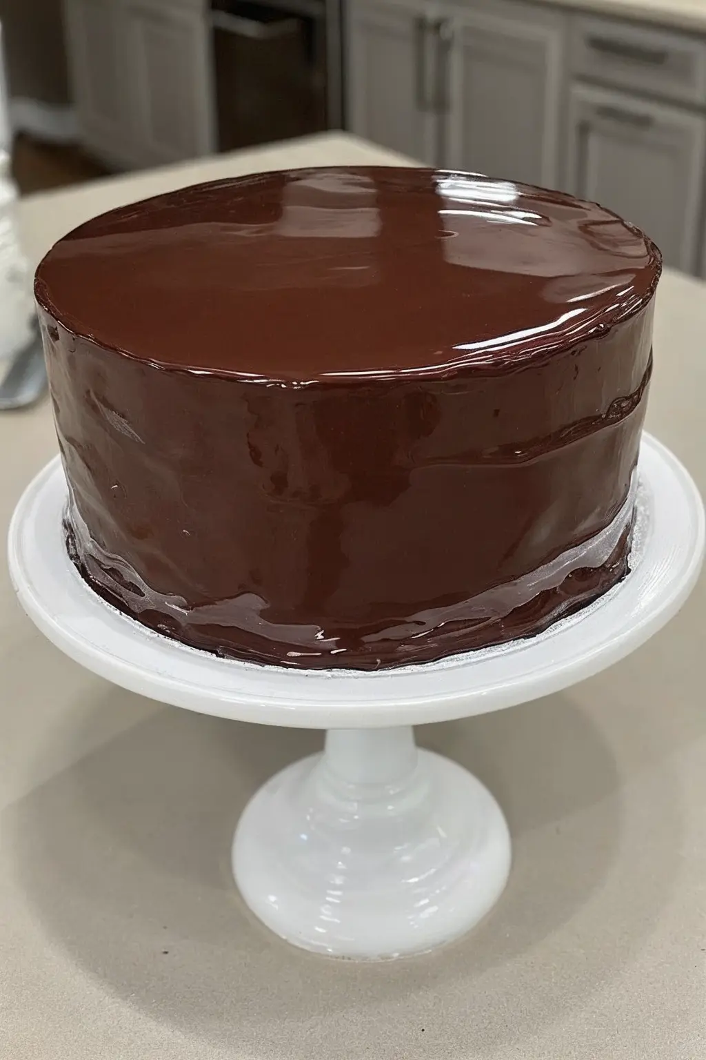 Glossy chocolate mirror glaze cake on a white stand with smooth, shiny surface